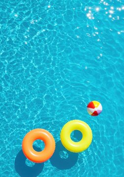 Colorful pool floaties and beach ball on clear blue water surface  