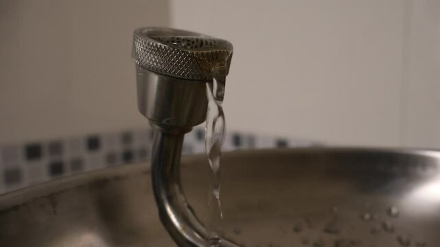 Close-up of a single nozzle on an emergency eyewash station with a gentle stream of water flowing into a stainless steel basin, typically used for eye safety in laboratories.