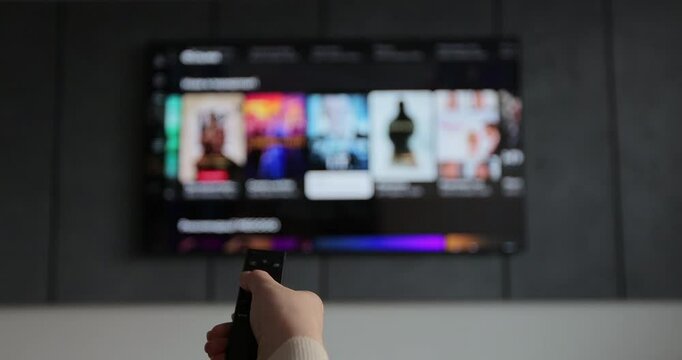 Woman hand operating a remote control for a smart TV. Channel surfing, focused on the hand and remote control. - Powered by Adobe
