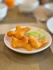 Golden crispy Thai 'Pa Thong Ko' (deep-fried dough sticks), a popular street food and breakfast item, served on a white plate with a sweet green pandan custard dip, perfect for Thai breakfast.