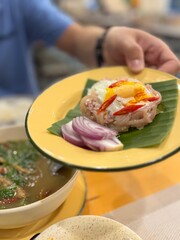 Authentic Thai 'Kua Naem' (stir-fried fermented pork with egg), a savory ,spicy Northern dish with a unique tangy flavor, served beautifully on a banana leaf with fresh red onion, a traditional Thai.