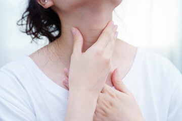 Asian woman touching her neck and throat for thyroid gland problem.