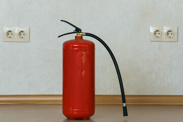 A fire extinguisher with a hose and a socket stands on the floor against the background of a wall...