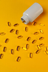 Fish oil capsules, omega 3, omega 9, pouring out of a medicine bottle on a yellow background with...