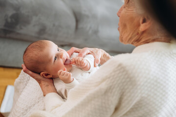 View from behind, holding toddler in hands. Grandmother with cute toddler baby at home