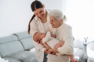 Obraz premium Cheerful facial expression. Mother, grandmother and little baby child on hands indoors