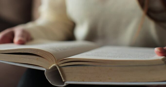 Woman reading a book and sitting on a sofa in front of the window. Learning, studying, education, read books, stay home concept.