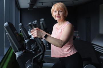 Fototapeta premium Senior woman training on elliptical machine in gym