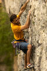 A man in a yellow shirt is climbing a rock wall