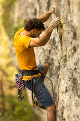 A man in a yellow shirt is climbing a rock wall