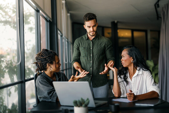 A manager frustrated addresses two employees during a work discussion in a modern office