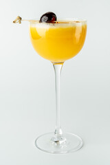 A vibrant yellow cocktail in a tall, elegant glass with a dark cherry garnish on a skewer, set against a clean white background, exuding a refreshing and sophisticated appeal.