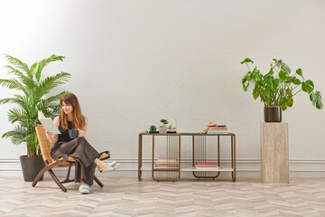 A woman is reading a book at home, looking at the phone and tablet. Decorative interior style and vase of plant.