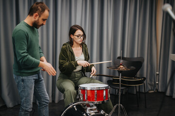 A music instructor teaching a student how to play drums during a band session in a studio. The...