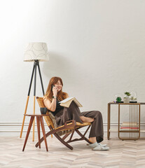 A woman is reading a book at home, looking at the phone and tablet. Decorative interior style and vase of plant.