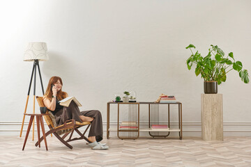 A woman is reading a book at home, looking at the phone and tablet. Decorative interior style and vase of plant.