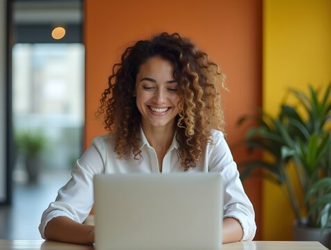 Young Female Communications Director Exuding Joy while Working on Laptop in Vibrant Office
