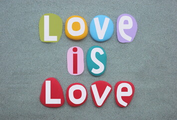 Love is love, social creative slogan composed with multi colored hand painted stone letters over green sand