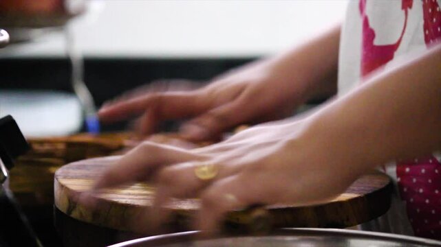 Close-up of hands skillfully rolling out dough to make traditional Indian roti or chapati on wooden board. Captures authentic home cooking, culinary traditions and fresh food.