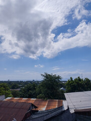 A peaceful rural town view with rusty metal roofs, lush green trees, and a partly cloudy blue sky in the background