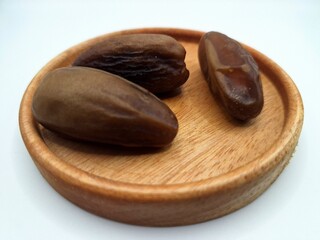 Date palm fruit on a small wooden plate. Date palm fruits, or simply dates, are the oval-shaped, sweet, edible fruit of the date palm tree (Phoenix dactylifera)