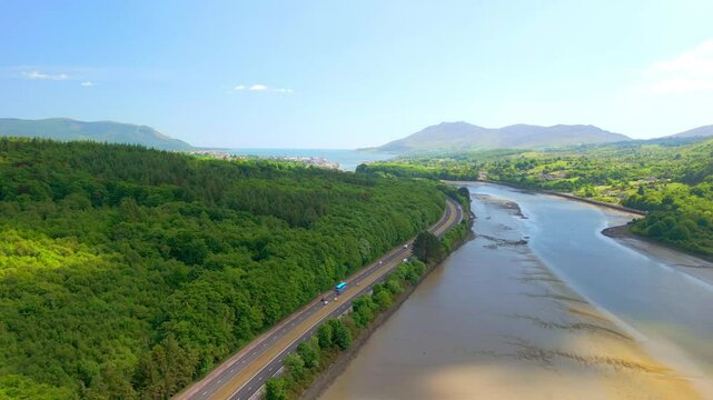 Wide, reversing aerial video of the Newry River and Mourne Mountains in Warrenpoint, County Down, Northern Ireland, UK on a bright and sunny day. Filmed in 4K, 60FPS and with Rec709 color.
