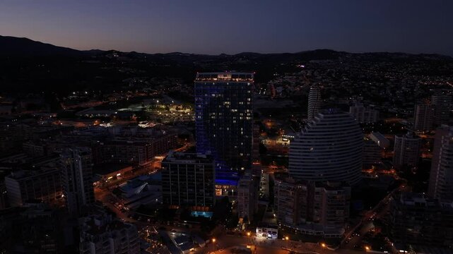 Amazing panoramic drone movement over Calp city buildings glowing under evening lights with Estimar hotel, Spain.
