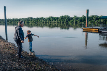 Grandfather teaching grandson how to fish on riverbank