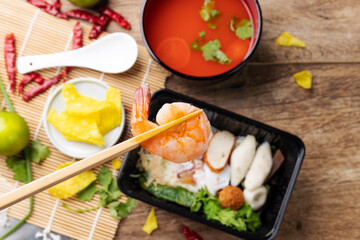 Chopsticks with fresh shrimp, seafood food with noodles and soup, close-up
