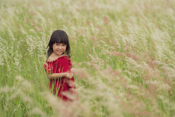 toddler girl in red dress playing grass flower in field