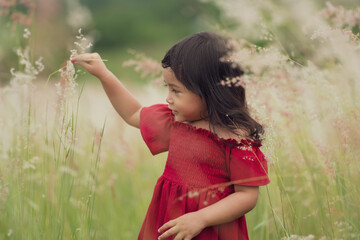 toddler girl in red dress playing grass flower in field