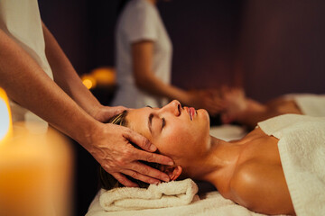 Young couple receiving massage in spa salon - Boyfriend and girlfriend wearing towels lying on massage tables at spa resort