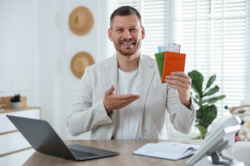 Travel agent with passports and tickets at wooden table in office