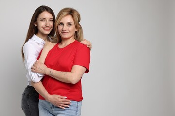 Woman hugging her mother on light grey background. Space for text
