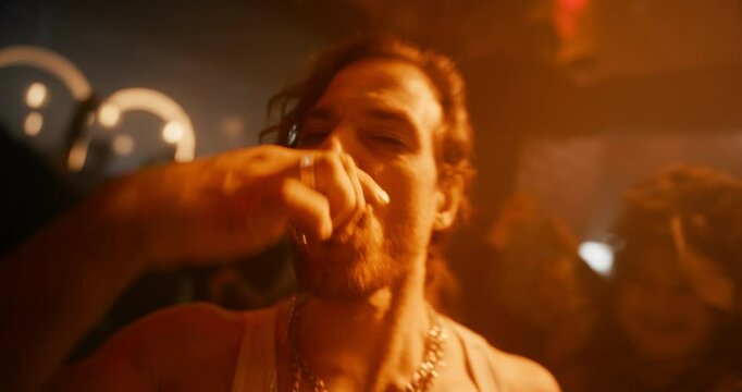 Lively Party Scene with a Stylish Caucasian Man Drinking Alcohol Shots and Kissing a Female While Walking Through a Diverse Male and Female Crowd at an Electronic Music Club Event