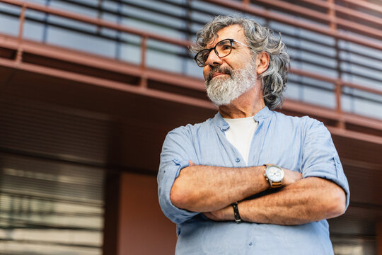 Thoughtful senior man standing with crossed arms looking to the side in the city