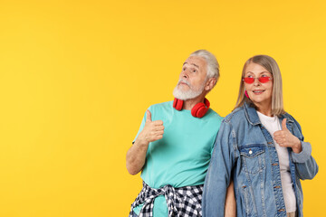 Senior couple in stylish outfits showing thumbs up on orange background, space for text