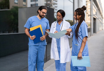 Multiethnic group of diverse healthcare professionals in uniforms reviewing documents outdoors