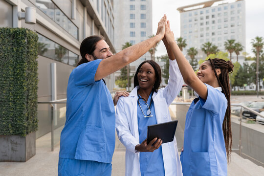 Diverse multiracial Doctors and nurses giving high five celebrating success outside hospital