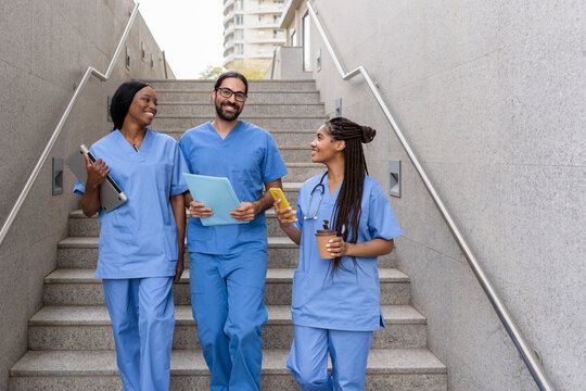 Medical diverse team walking down stairs holding medical records, laptop, smartphone and coffee