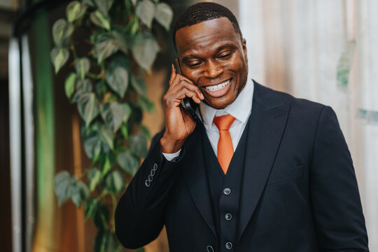 An individual dressed in formal business wear smiles while speaking on a mobile phone, depicting effective communication in a contemporary office setting.