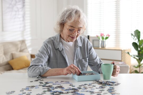 Woman with cup of drink solving jigsaw puzzle at white table indoors