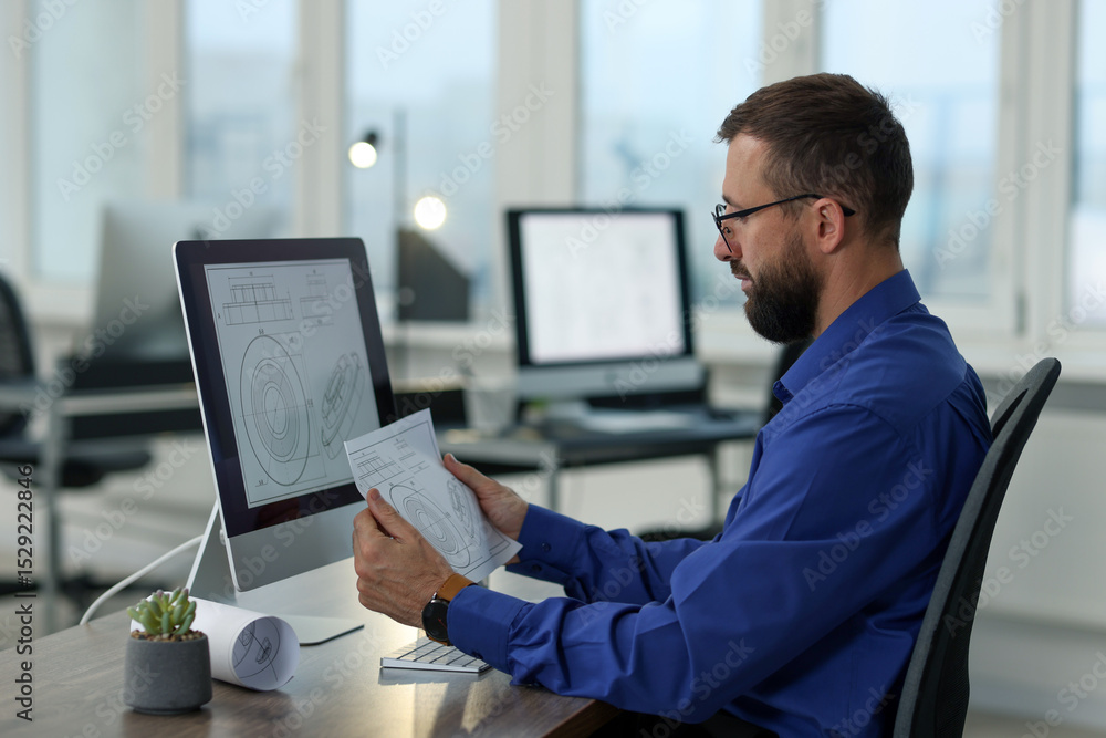 Poster technician making digital engineering drawing on computer at desk in office