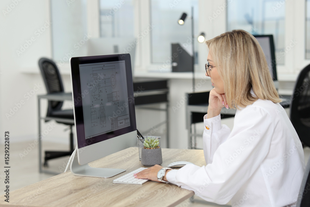 Poster technician making digital engineering drawing on computer at desk in office