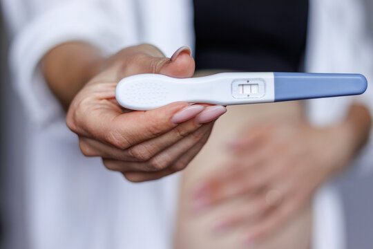 Blurred woman holding pregnancy test with focus on test. Concept of early pregnancy, motherhood, fertility and women's health. Indoor, natural light