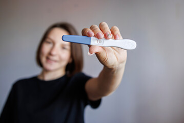 Young woman holding pregnancy test with focus on test. Concept of early pregnancy, motherhood,...