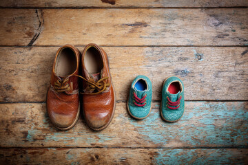 Worn brown leather shoes and small baby shoes on wooden floor, symbolizing family and growth