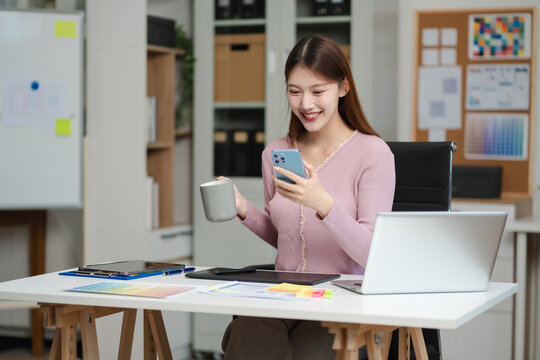 Female coder or developer working  using a smartphone and computer display in problem solving at workplace.