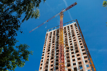 A high rise apartment building under construction, surrounded by trees, with a crane on the roof, under a clear blue sky.