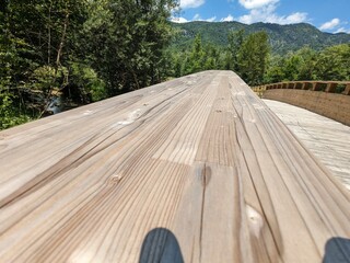Wooden pedestrian bridge crossing a river in a scenic valley surrounded by Austrian Alps mountain peaks.